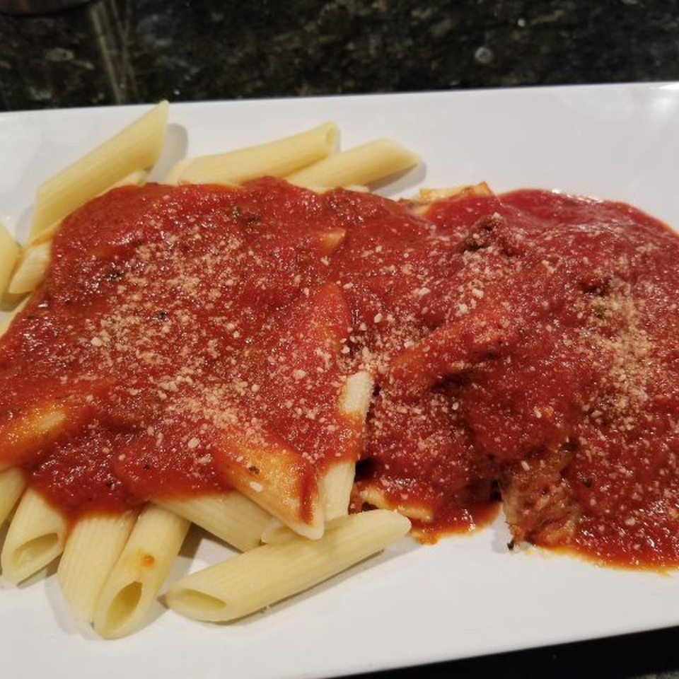 Penne pasta with rich red marinara sauce and grated Parmesan cheese on a white plate.