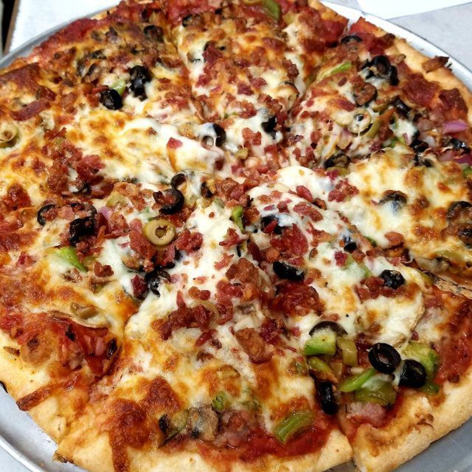 A close-up of a Bravo Pizza & Italian Restaurant pizza with bacon, olives, and green peppers.