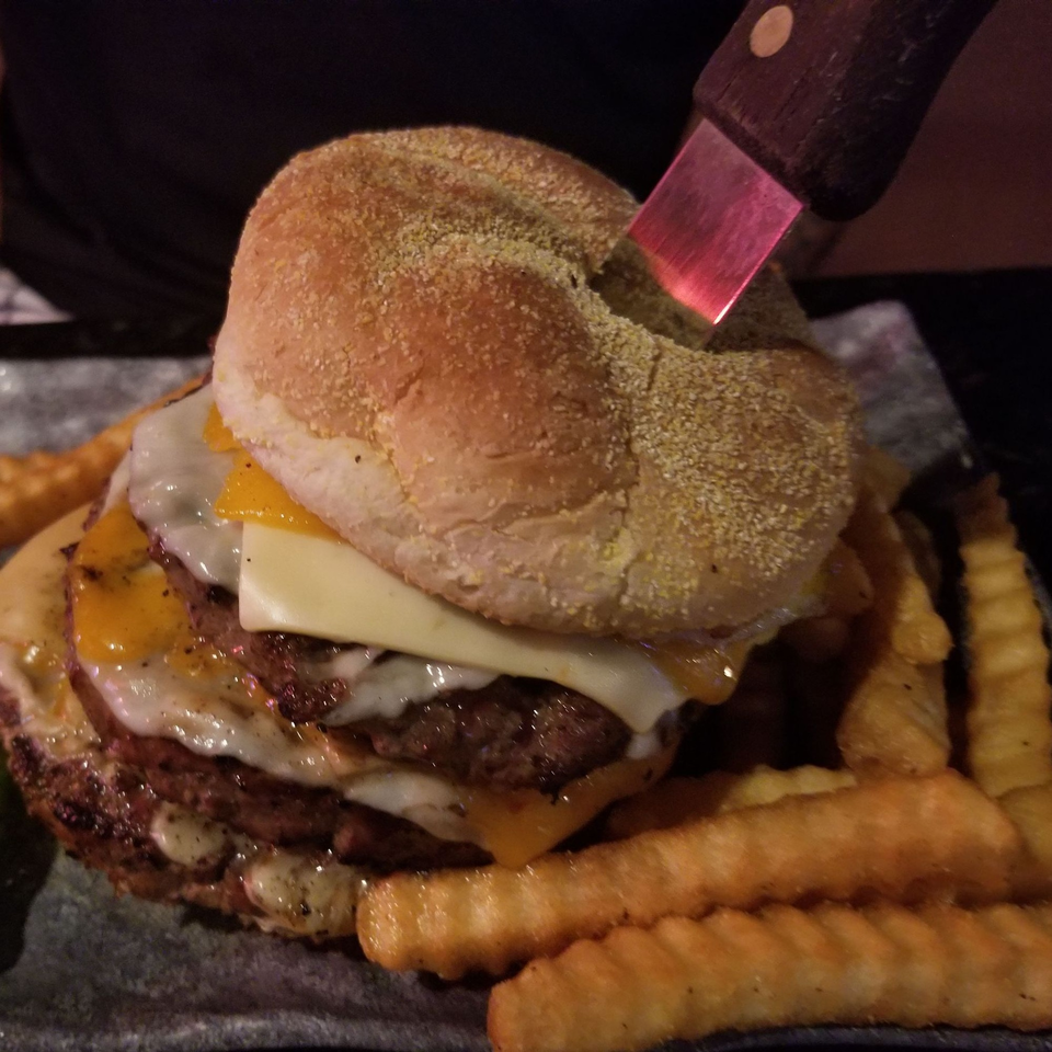 A large double cheeseburger with melted cheese and a knife stuck in the bun, served with crinkle-cut fries.
