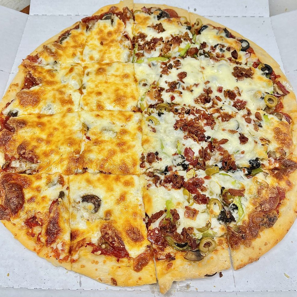 A large, round Bravo Pizza with various toppings, including cheese, pepperoni, olives, and bacon.